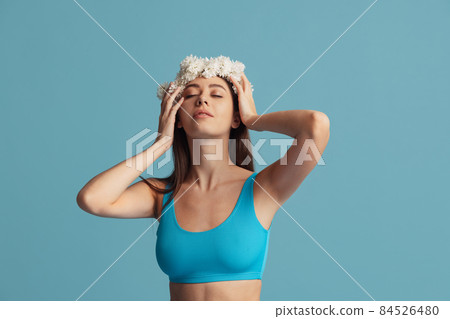 Pretty charming girl in wreath of flowers posing isolated over blue color studio background. Natural beauty concept. 84526480