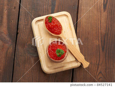 red caviar of pink salmon lies in a wooden spoon on a cutting board. Brown wooden table red caviar of pink salmon lies in a wooden spoon on a cutting board. Brown wooden table 84527141