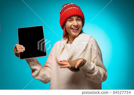 Cropped portrait of young girl pointing at tablet screen isolated over blue background Cropped portrait of young girl pointing at tablet screen isolated over blue background 84527754