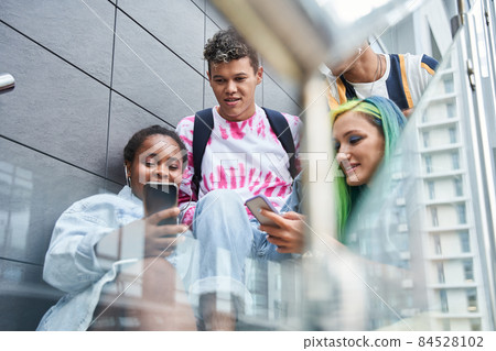 Friends sitting and watching something on phones 84528102