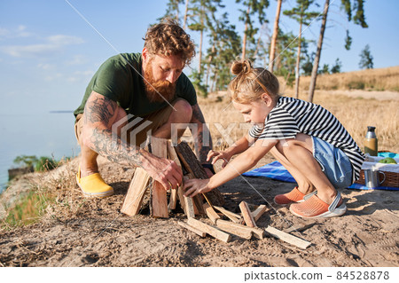 Father and daughter making fire from logs on coast 84528878