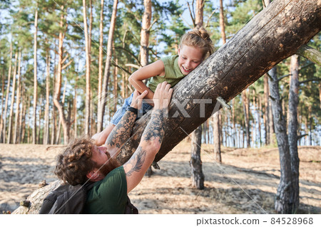 Man holding his daughter on fallen tree in forest 84528968