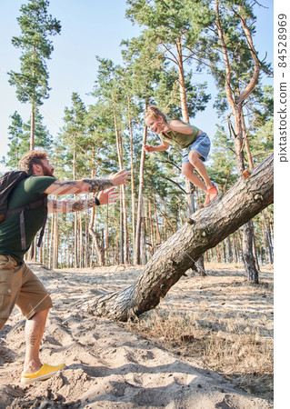 Girl jumping from fallen tree on sand in forest 84528969