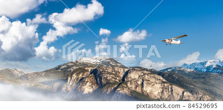 Airplane flying over the mountain landscape during cloudy day. 84529695