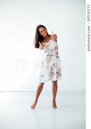 brunette woman in a summer dress in a white room brunette woman in a summer dress in a white room 84530231