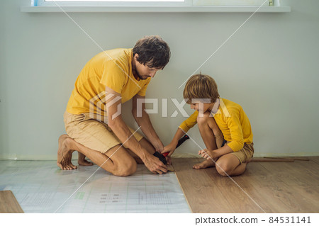 Father and son installing new wooden laminate flooring on a warm film floor. Infrared floor heating system under laminate floor Father and son installing new wooden laminate flooring on a warm film floor. Infrared floor heating system under laminate floor 84531141