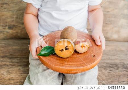 Hands holding a board with fresh sapodilla fruits on old wooden background Hands holding a board with fresh sapodilla fruits on old wooden background 84531850