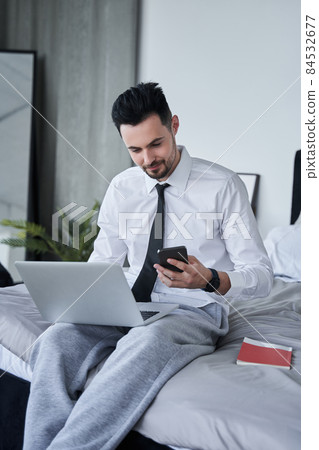 Man sitting at the bed and checking something at his mobile device while working 84532677
