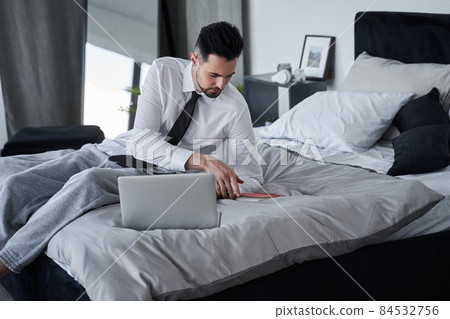 Man laying at the bed and reading something at his notebook while preparing to the work 84532756