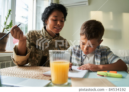 Black mother looking at son writing in notebook Black mother looking at son writing in notebook 84534192