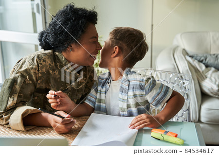 Soldier woman laughing out loud while drawing at the table with her little son Soldier woman laughing out loud while drawing at the table with her little son 84534617