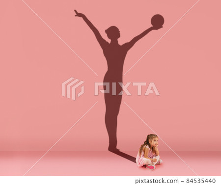 Conceptual image with kid, little girl and shadow of female gymnast on studio pink wall. Dreams about sport career 84535440