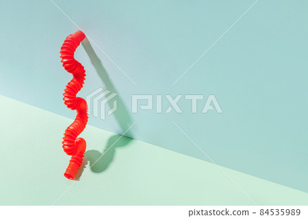 The curved pop tube stands leaning against the wall. Modern still life with antistress toy The curved pop tube stands leaning against the wall. Modern still life with antistress toy 84535989