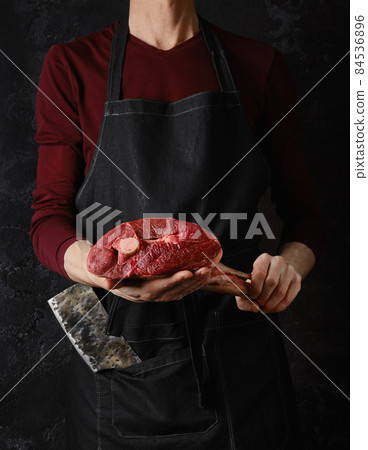 Butcher holds raw lamb leg in hands over black background Butcher holds raw lamb leg in hands over black background 84536896