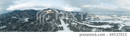 Aerial shot of majestic sunrise in the mountains. Valley between the mountains is covered with fog and is illuminated by the warm rays of the rising sun. Mountains covered with forest natural. Aerial shot of majestic sunrise in the mountains. Valley between the mountains is covered with fog and is illuminated by the warm rays of the rising sun. Mountains covered with forest natural. 84537015