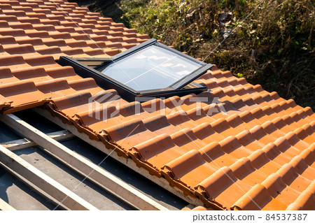 Overlapping rows of yellow ceramic roofing tiles mounted on wooden boards covering residential building roof under construction. 84537387