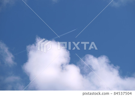 Distant passenger jet plane flying on high altitude on blue sky with white clouds leaving smoke trace of contrail behind. Air traveling concept. 84537504
