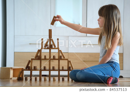 Creative child girl playing with game stacking wooden toy blocks in high building structure. Hand movement control and concentration skills concept 84537513