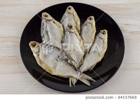 beer snack: 6 sun-dried freshwater salt fish on black plate - a source of vitamins and protein, gray table, placed in the shape of a maple leaf 84537668