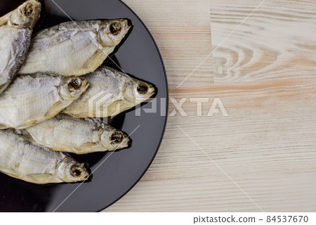 beer snack: 6 sun-dried freshwater salt fish on black plate - a source of vitamins and protein, gray table, location right 84537670