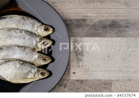 beer snack: 4 sun-dried freshwater salt fish on black plate in a row - a source of vitamins and protein, gray table, free space 84537674