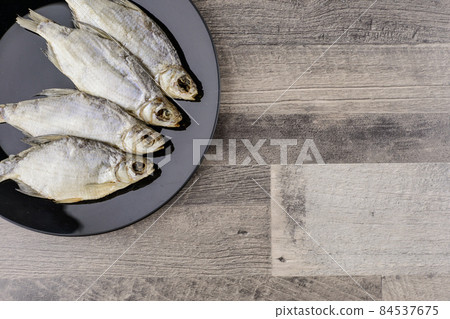 beer snack: 4 sun-dried freshwater salt fish on black plate - a source of vitamins and protein, grey table, free space 84537675