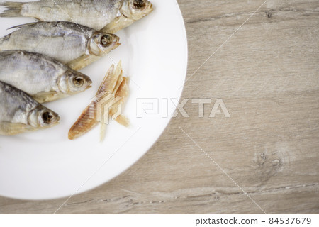 beer snack: 4 sun-dried salted freshwater fish on a white plate - a source of vitamins and protein, a few peeled slices of meat, light table, location right 84537679