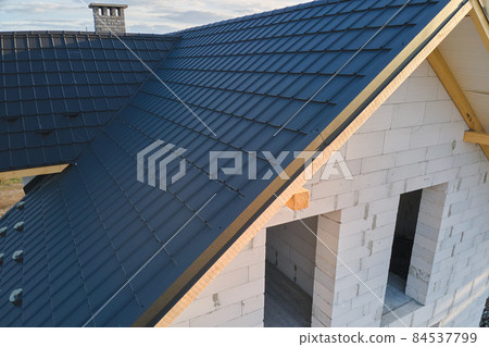 Aerial view of unfinished house with aerated lightweight concrete walls and wooden roof frame covered with metallic tiles under construction. 84537799