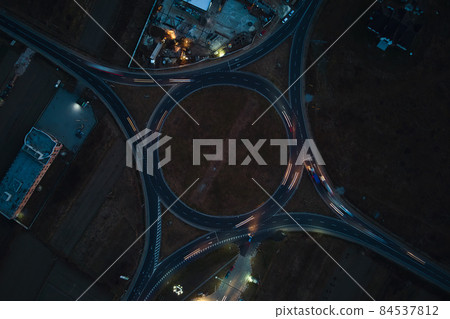 Aerial view of road roundabout intersection with fast moving heavy traffic at night. Top view of urban circular transportation crossroads. Rush hour with blurred car trail lights 84537812