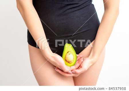 Young woman holding one half of a fresh avocado fruit close to her belly against a white background, healthy nutrition and pregnancy concept. 84537938