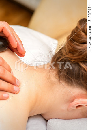 Hot stone massage therapy. Caucasian young woman getting a hot stone massage on back at spa salon. 84537954