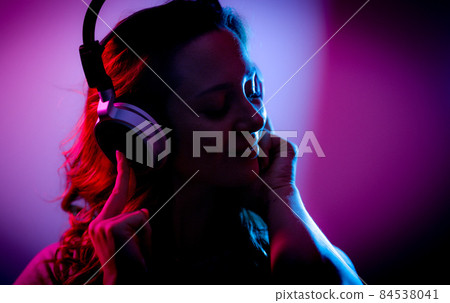 Young woman listens to music on her headphones - stylish illuminated Young woman listens to music on her headphones - stylish illuminated 84538041