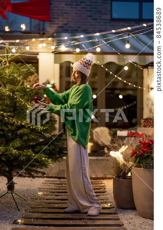 Woman decorating Christmas tree at backyard Woman decorating Christmas tree at backyard 84538689