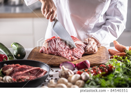 Chef cuts a slice from a chunk of red meat by a big knife in the restaurant Chef cuts a slice from a chunk of red meat by a big knife in the restaurant 84540351