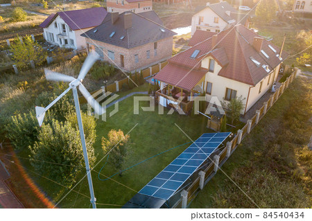 Aerial view of a residential private house with solar panels on roof and wind generator turbine. 84540434