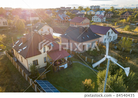 Aerial view of a residential private house with solar panels on roof and wind generator turbine. 84540435
