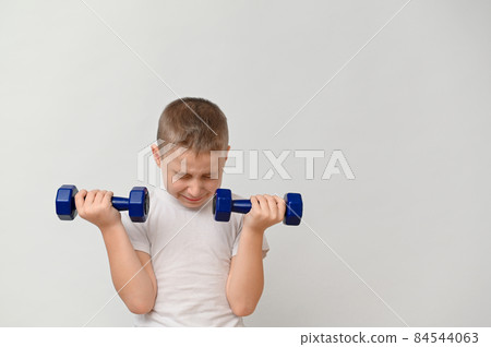 a boy 8-10 years old with dumbbells on a white background. the boy is doing sports, it's hard for him, he's tired and closed his eyes. copy space a boy 8-10 years old with dumbbells on a white background. the boy is doing sports, it's hard for him, he's tired and closed his eyes. copy space 84544063