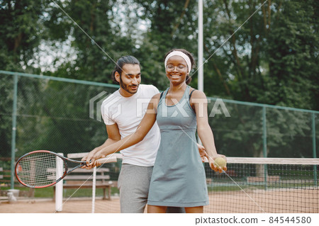 Man teaching a woman how to play tennis 84544580