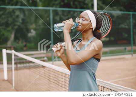 Black american female tennis player drinking water on the court outdoors 84544581