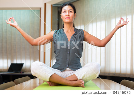 Businesswoman sitting at the table in lotus position Businesswoman sitting at the table in lotus position 84546075
