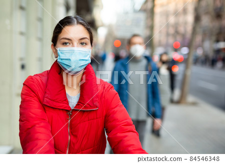 Young woman wearing face mask walks along city street Young woman wearing face mask walks along city street 84546348
