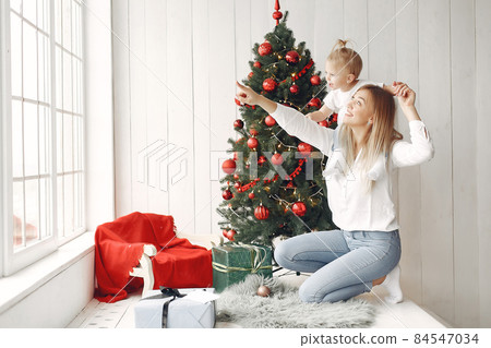 Mother with little daughter sitting by the Christmas tree and having fun. 84547034