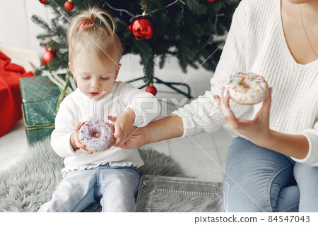 Mother with little daughter sitting near Christmas tree and and go donuts. Mother with little daughter sitting near Christmas tree and and go donuts. 84547043