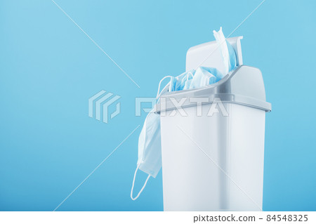 A white trash can full of virus protection masks on a blue background. A white trash can full of virus protection masks on a blue background. 84548325