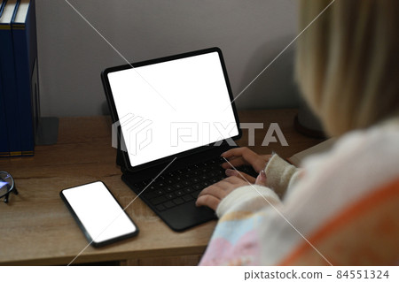 Over shoulder view of young woman using computer tablet a home. 84551324