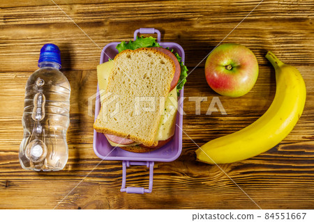 Lunch box with sandwiches, bottle of water, banana and apple on a wooden table. Top view Lunch box with sandwiches, bottle of water, banana and apple on a wooden table. Top view 84551667
