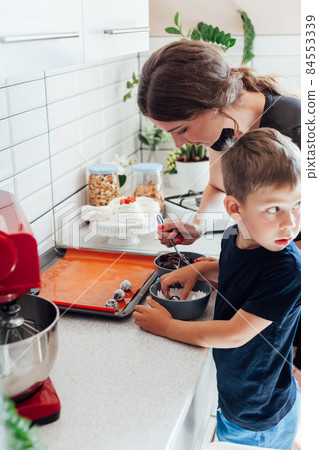a woman with her son cooks delicious sweet dessert cakes in the kitchen a woman with her son cooks delicious sweet dessert cakes in the kitchen 84553339
