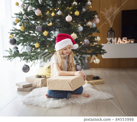 A girl with gifts plays near the Christmas tree. A girl with gifts plays near the Christmas tree. 84553998