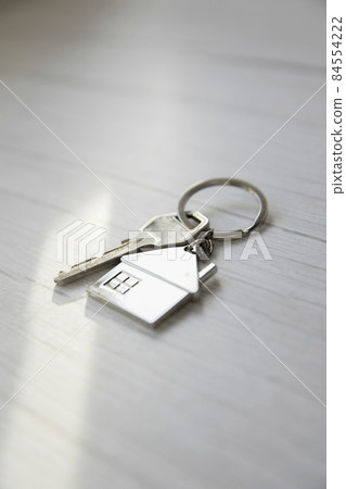 Silver key with silver house figure on white wooden background, buying new house real estate concept copy space 84554222