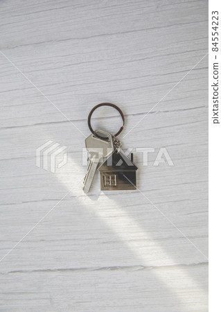 Silver key with silver house figure on white wooden background, buying new house real estate concept copy space 84554223
